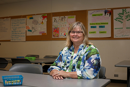 Beth Marshall, WCC's Early Childhood Program Coordinator and Faculty, sits in front of childhood development posters her students created.